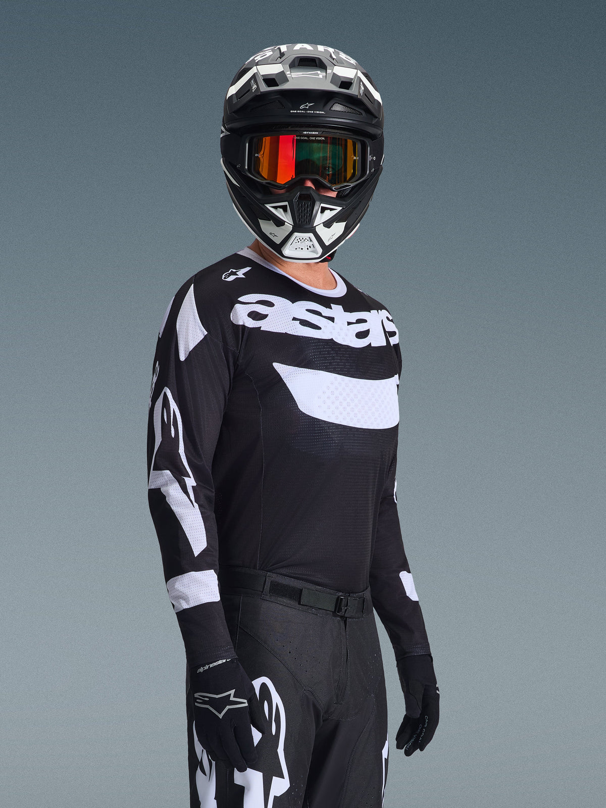 Motocross-Fahrer trägt das 2026 Racer Air Riway Trikot, schwarz-weißes Trikot mit „astars“-Logo, passender schwarz-weißer Helm mit orange verspiegelter Brille, schwarze Motocross-Hose und Handschuhe, abgestimmtes Outfit für den Offroad-Rennsport