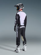 Motocross-Fahrer in der Rückansicht mit dem 2026 Racer Air Riway Jersey in Schwarz und Weiß, zeigt den großen weißen Mesh-Rückeneinsatz für optimale Belüftung, kombiniert mit schwarzer Hose, schwarz-weißem Helm und weißen Rennstiefeln, komplette Profi-Ausrüstung für Offroad-Performance.