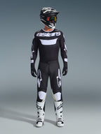 Motocross-Fahrer in kompletter Rennausrüstung, Alpinestars 2026 Racer Air Riway Trikot in Schwarz und Weiß mit „astars“-Logo auf der Brust, passende schwarze Hose mit weißen Akzenten, weiße Motocross-Stiefel und schwarz-weißer Helm mit Brille, professionell abgestimmtes Offroad-Outfit
