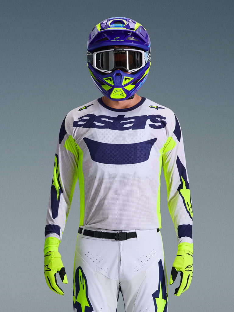 Alpinestars 2026 Racer Air Riway Jersey, Light Gray with Dark Blue astars logo, Fluo Yellow and Blue accents on sleeves, worn by a motocross rider with matching purple and neon yellow helmet and gloves, technical mesh fabric for off-road racing.