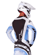 Rückansicht eines Motocross-Fahrers im Alpinestars 2025 Techstar Melt Gear Set in Weiß und Blau, Trikot mit großem schwarzem Rückenteil, weißem Stern-Logo und hellblauen Ärmeln mit Farbverlauf, dazu passende weiß-blaue Hose, weißer Rennhelm und schwarz-weiße Handschuhe, abgestimmte Performance-Ausrüstung für Motocross
