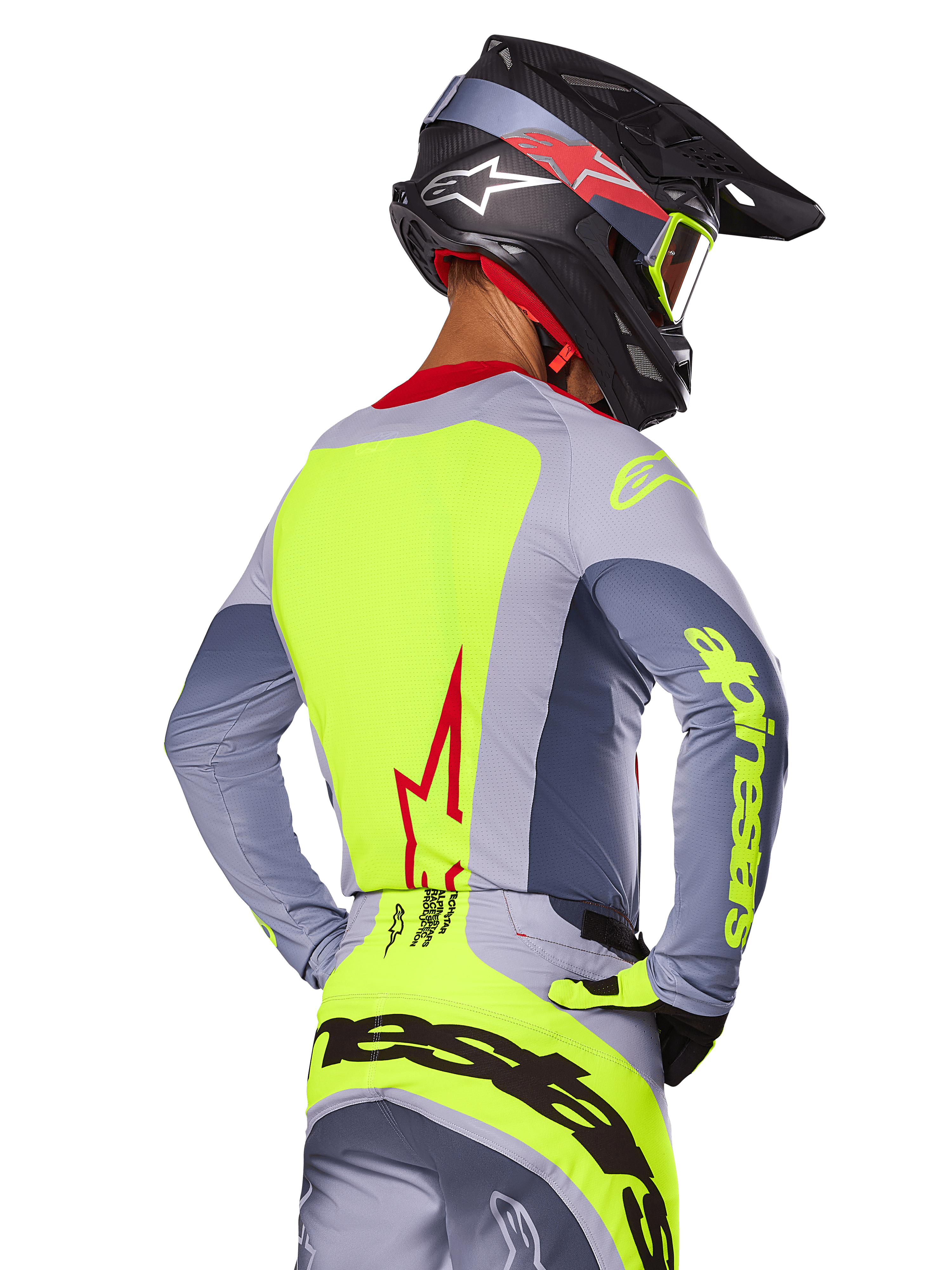 Alpinestars 2025 Techstar Melt Trikot, Bright Red Gray, Rückansicht eines Motocross-Fahrers in grauer und neongelber Rennausrüstung, rotes Stern-Logo auf dem Rücken, passender schwarz-roter Helm, Performance-Offroad-Bekleidung