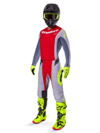 Motocross-Fahrer trägt das Alpinestars 2025 Techstar Melt Jersey in Hellrot und Grau, mit einer roten Brustpartie und grauen Ärmeln mit neongelben Akzenten. Kombiniert mit der passenden Hose, leuchtend gelben Rennstiefeln und Handschuhen sowie einem schwarzen Helm mit gelb gerahmter Goggle für eine komplette Offroad-Rennausrüstung.