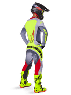 Motocross-Fahrer von hinten im Alpinestars 2025 Techstar Melt Jersey in Bright Red Gray, mit leuchtend gelber Rückenpartie und grauen Ärmeln, dazu passende grau-rote Hose mit gelbem Branding, leuchtend gelbe Motocross-Stiefel und schwarzer Helm mit gelber Motocross-Brille, koordinierte Offroad-Rennausrüstung