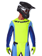 Alpinestars 2025 Techstar Melt Trikot, Motocross-Renn-Trikot, Gelb Fluo und Blau, mit lasergeschnittener Belüftung und athletischer Rennpassform, getragen von einem Fahrer mit schwarzem Helm und gelben Fluo-Handschuhen