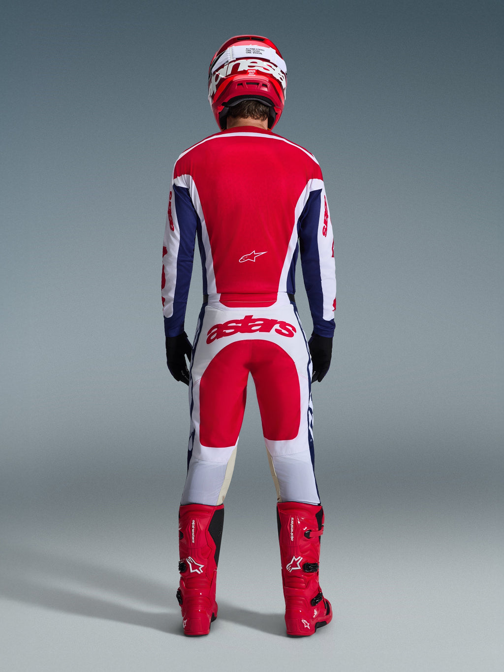 Motocross-Fahrer in der Rückansicht mit dem 2026 Racer Riway Ausrüstungsset, rot-blaues Trikot mit weißen Akzenten, weiße Hose mit roten Einsätzen und „astars“-Logo am Gesäß, kombiniert mit einem roten Helm, roten Stiefeln und schwarzen Handschuhen, Hochleistungs-Rennausrüstung für den Offroad-Einsatz