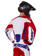 Alpinestars 2025 Racer Veil Trikot und Hose, Motocross-Ausrüstungsset, Hellrot, Weiß und Blau, Rückansicht eines Fahrers in passender Ausrüstung und schwarzem Motocross-Helm, mit markantem blauem Alpinestars-Branding, technische Offroad-Rennbekleidung
