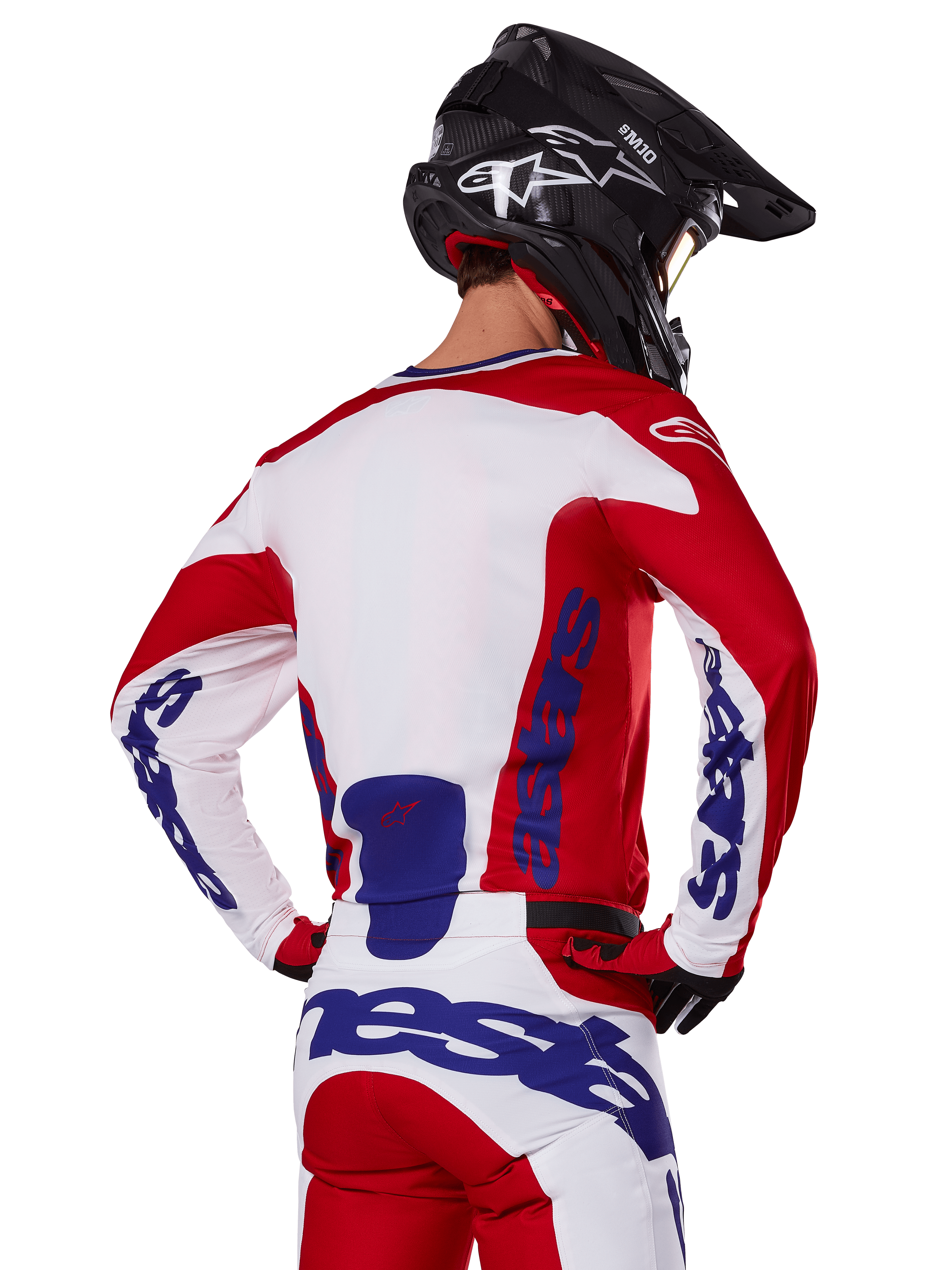Alpinestars 2025 Racer Veil Trikot und Hose, Motocross-Ausrüstungsset, Hellrot, Weiß und Blau, Rückansicht eines Fahrers in passender Ausrüstung und schwarzem Motocross-Helm, mit markantem blauem Alpinestars-Branding, technische Offroad-Rennbekleidung
