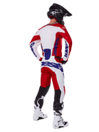 Motocross-Fahrer in der Rückansicht, trägt das Alpinestars 2025 Racer Veil Trikot und die Hose in Rot und Weiß, mit blauem Branding, schwarzem Helm und weißen Stiefeln, komplettes Ausrüstungsset für Offroad-Rennen