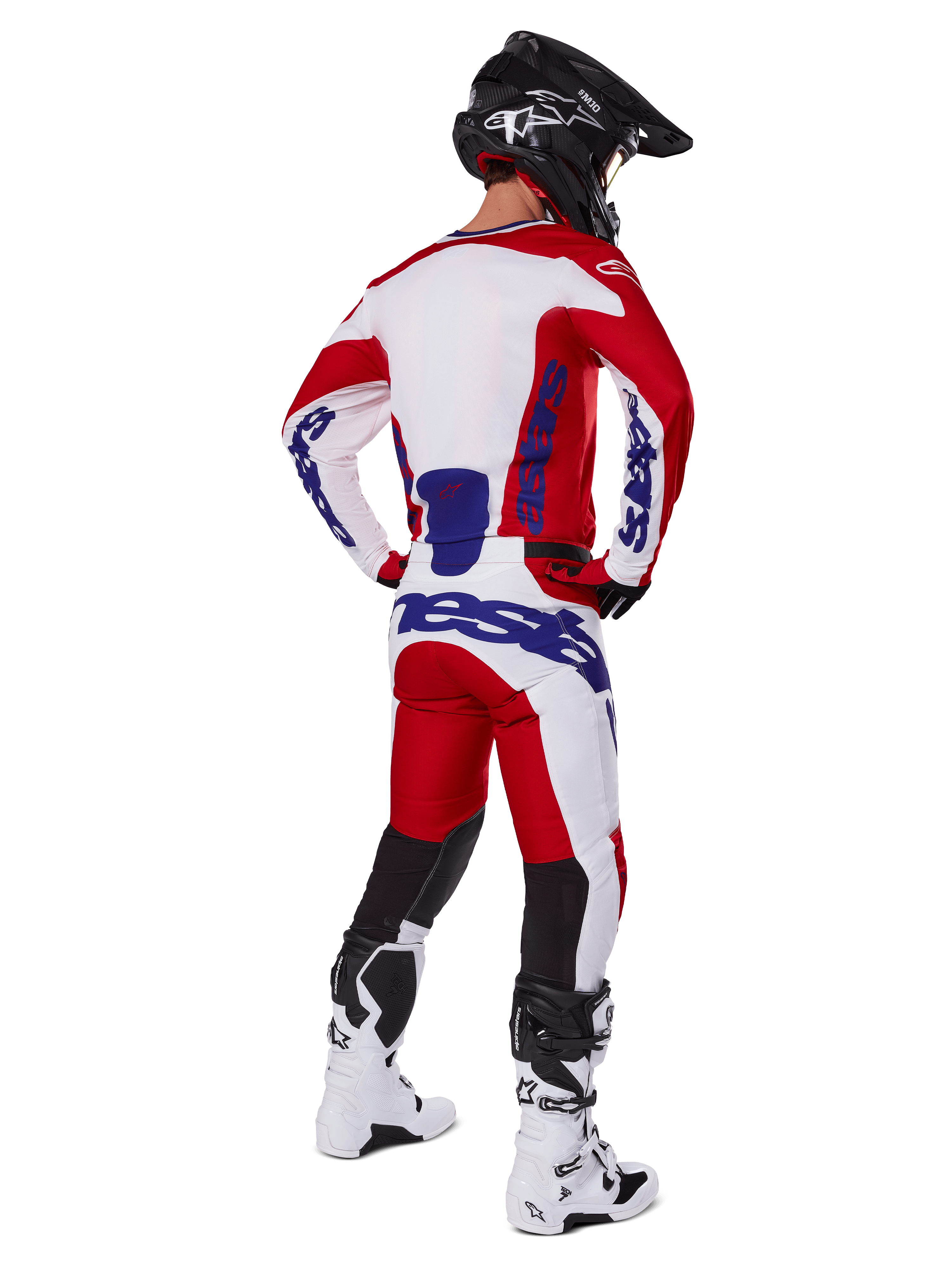 Motocross-Fahrer in der Rückansicht, trägt das Alpinestars 2025 Racer Veil Trikot und die Hose in Rot und Weiß, mit blauem Branding, schwarzem Helm und weißen Stiefeln, komplettes Ausrüstungsset für Offroad-Rennen