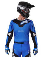 Alpinestars 2025 Racer Veil Jersey, Motocross-Trikot, Blau und Schwarz, getragen mit passender Motocross-Ausrüstung einschließlich Helm und Handschuhen, sportliches Design mit weißem Alpinestars-Branding