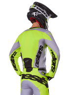 Motocross-Fahrer von hinten im Alpinestars 2025 Racer Veil Trikot in Grau und Gelb Fluo, mit markantem „astars“-Branding auf dem Rücken und den Ärmeln, kombiniert mit der passenden Hose und einem schwarzen Helm für einen kompletten Racing-Look.