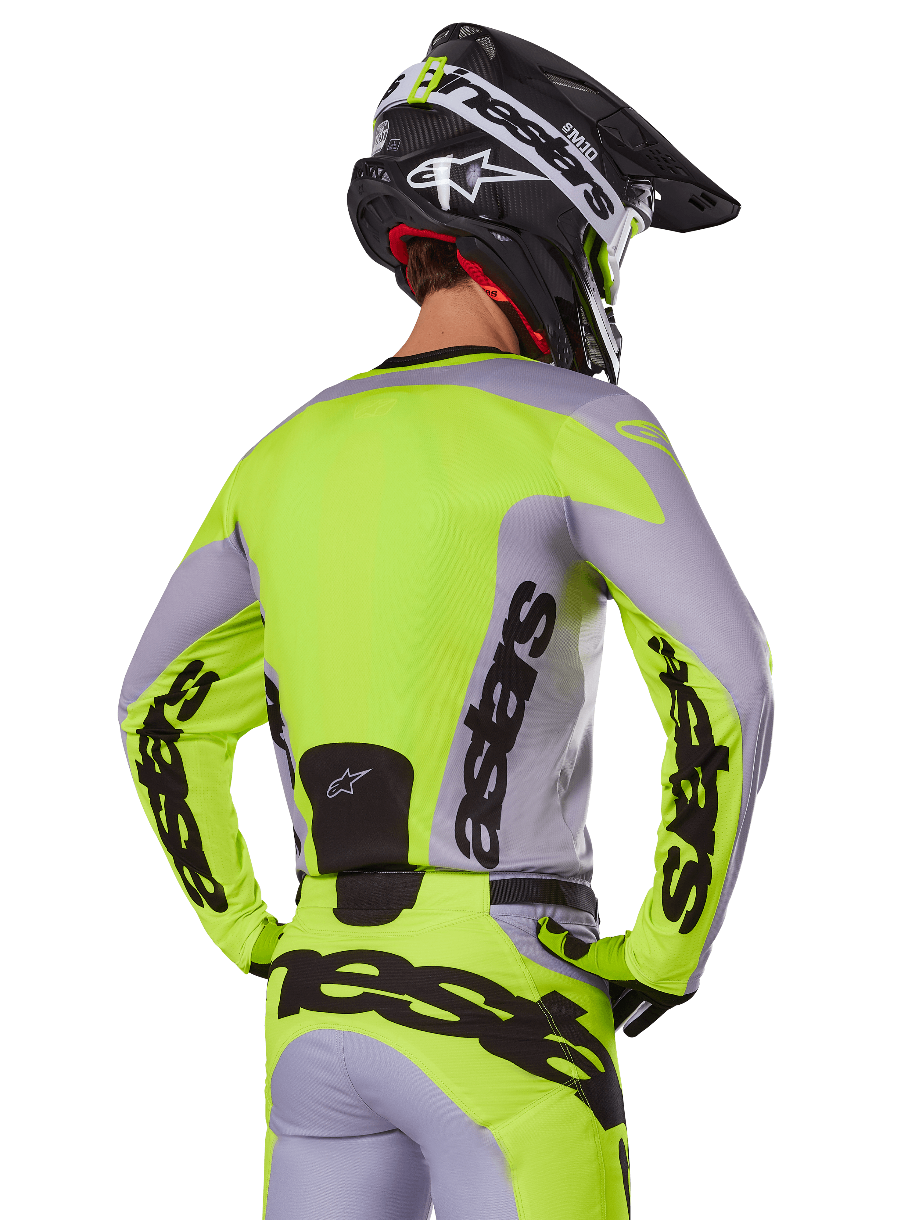 Motocross-Fahrer von hinten im Alpinestars 2025 Racer Veil Trikot in Grau und Gelb Fluo, mit markantem „astars“-Branding auf dem Rücken und den Ärmeln, kombiniert mit der passenden Hose und einem schwarzen Helm für einen kompletten Racing-Look.