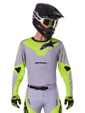 Alpinestars 2025 Racer Veil Jersey, Motocross-Trikot, Grau und Neongelb, langärmliges Design mit schwarzen Alpinestars-Logos, gezeigt als Teil eines kompletten Rennausrüstungs-Sets mit passender Hose, schwarzem Helm und Handschuhen