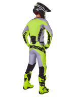 Motocross-Fahrer von hinten im Alpinestars 2025 Racer Veil Gear Set, Trikot und Hose in Grau und Gelb Fluo, passende fluorgelbe Stiefel und schwarz-gelber Helm, koordinierte Ausrüstung für den Offroad-Rennsport
