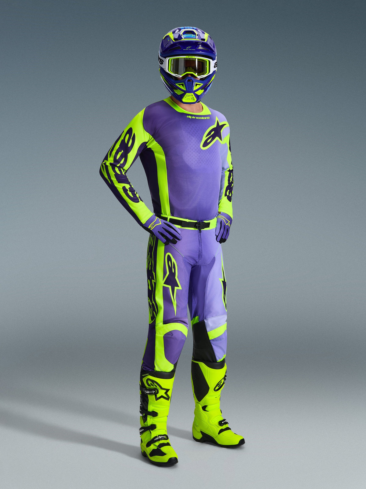 Motocross-Fahrer in kompletter Alpinestars Ausrüstung, 2026 Racer Portl Trikot und passende Hose in Lila und Gelb Fluo, kombiniert mit passendem Helm, Brille und lila Handschuhen, leuchtend neongelbe Offroad-Stiefel, professionelles Renn-Outfit für Motocross-Performance.