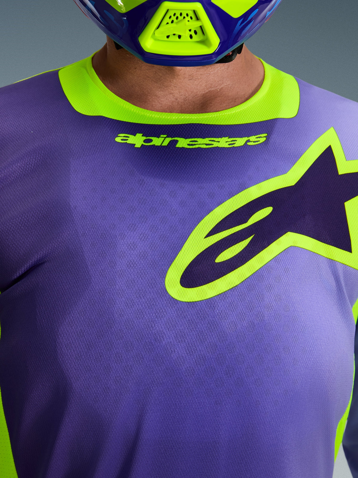 Alpinestars 2026 Racer Portl Trikot, Motocross-Trikot, Lila und Gelb Fluo, Nahaufnahme des Brustbereichs mit einem großen gelb umrandeten Alpinestars-Logo, Stretch-Kragen mit Branding, technisches feuchtigkeitsableitendes Polygewebe