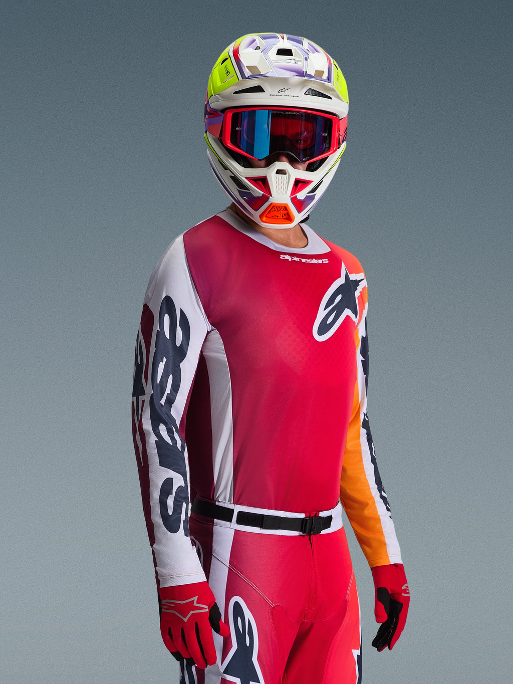 Motocross-Fahrer im Alpinestars 2026 Racer Portl Jersey, Rot mit weißen und dunkelgrauen Ärmeln, dazu passende Motocross-Hose, mehrfarbiger Helm mit blauer Brille und rote Handschuhe, Studioaufnahme