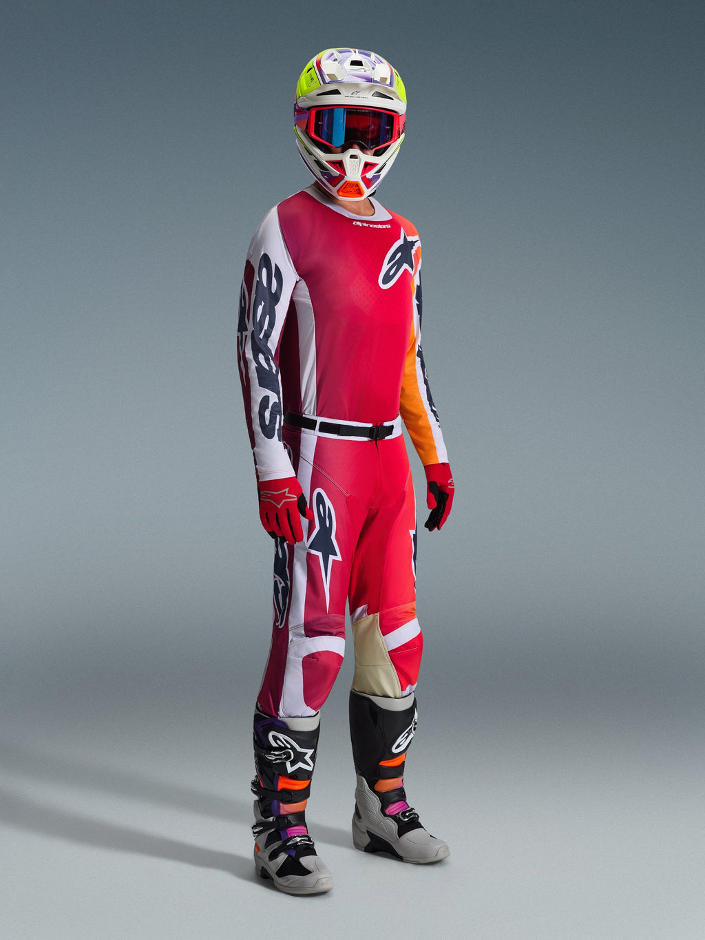 Motocross-Fahrer in kompletter Rennausrüstung, Alpinestars 2026 Racer Portl Trikot in Rot und Hellgrau, passende Motocross-Hose mit weißen und dunkelgrünen Akzenten, mehrfarbiger Helm mit roter Goggle, grau-schwarze Stiefel mit orangefarbenen und lila Details, rote Handschuhe, aufeinander abgestimmtes Outfit für Offroad-Rennen