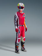 Motocross-Fahrer in kompletter Rennausrüstung, Alpinestars 2026 Racer Portl Trikot in Rot und Hellgrau, passende Motocross-Hose mit weißen und dunkelgrünen Akzenten, mehrfarbiger Helm mit roter Goggle, grau-schwarze Stiefel mit orangefarbenen und lila Details, rote Handschuhe, aufeinander abgestimmtes Outfit für Offroad-Rennen
