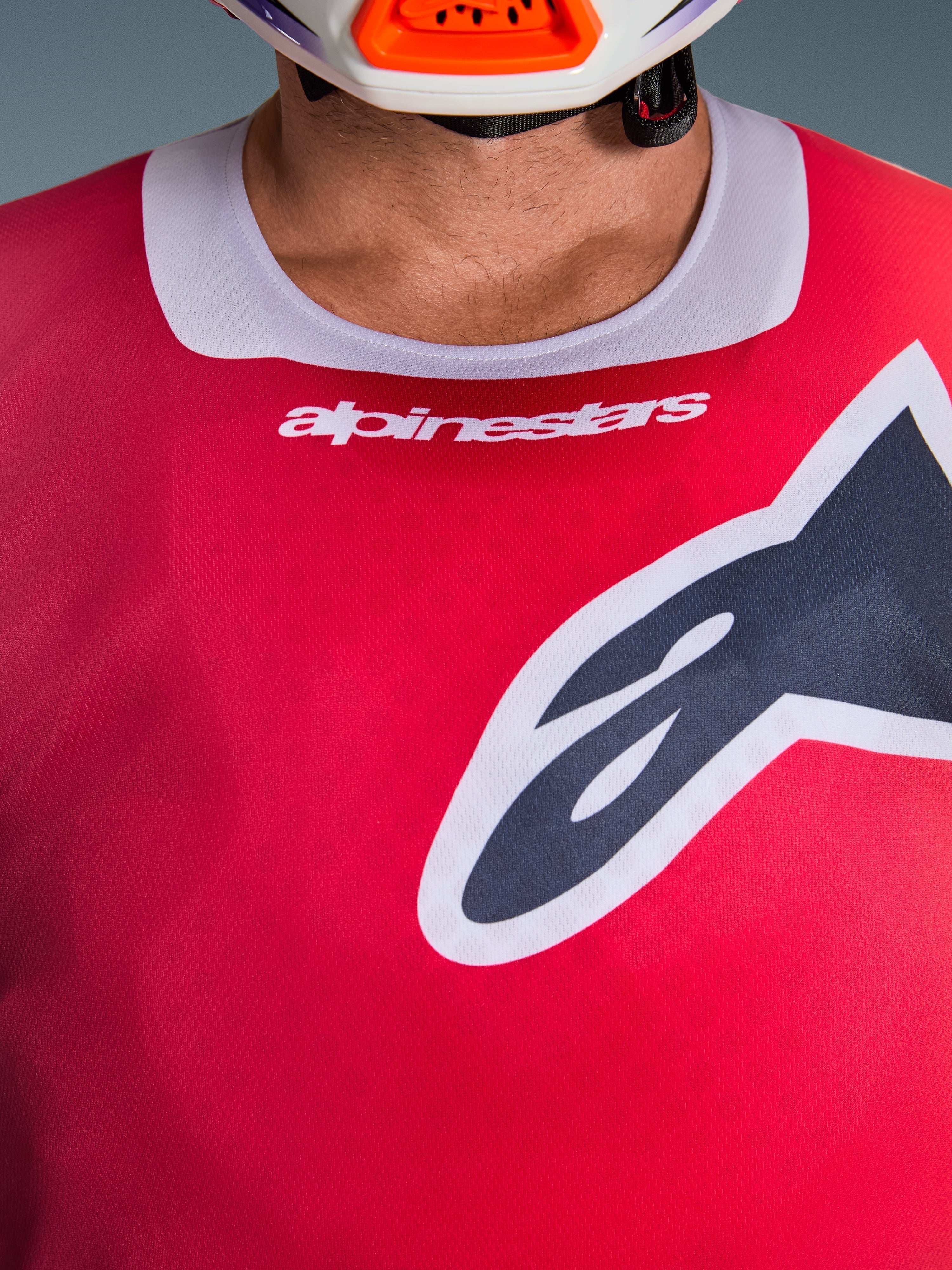 Alpinestars 2026 Racer Portl Jersey, close-up view of the chest and collar area, Red with Light Gray neck trim, white Alpinestars text and large Astars logo, featuring a moisture-wicking technical fabric texture