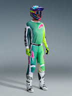 Motocross-Fahrer in kompletter Rennausrüstung, 2026 Racer Portl Trikot in Grün mit weiß-schwarzen Ärmeln und pinkfarbenem Logo, passende grüne Hose mit pinkfarbenen Akzenten, mehrfarbiger Helm mit Brille, weiß-schwarze Stiefel und grüne Handschuhe, abgestimmtes Outfit für den Offroad-Rennsport