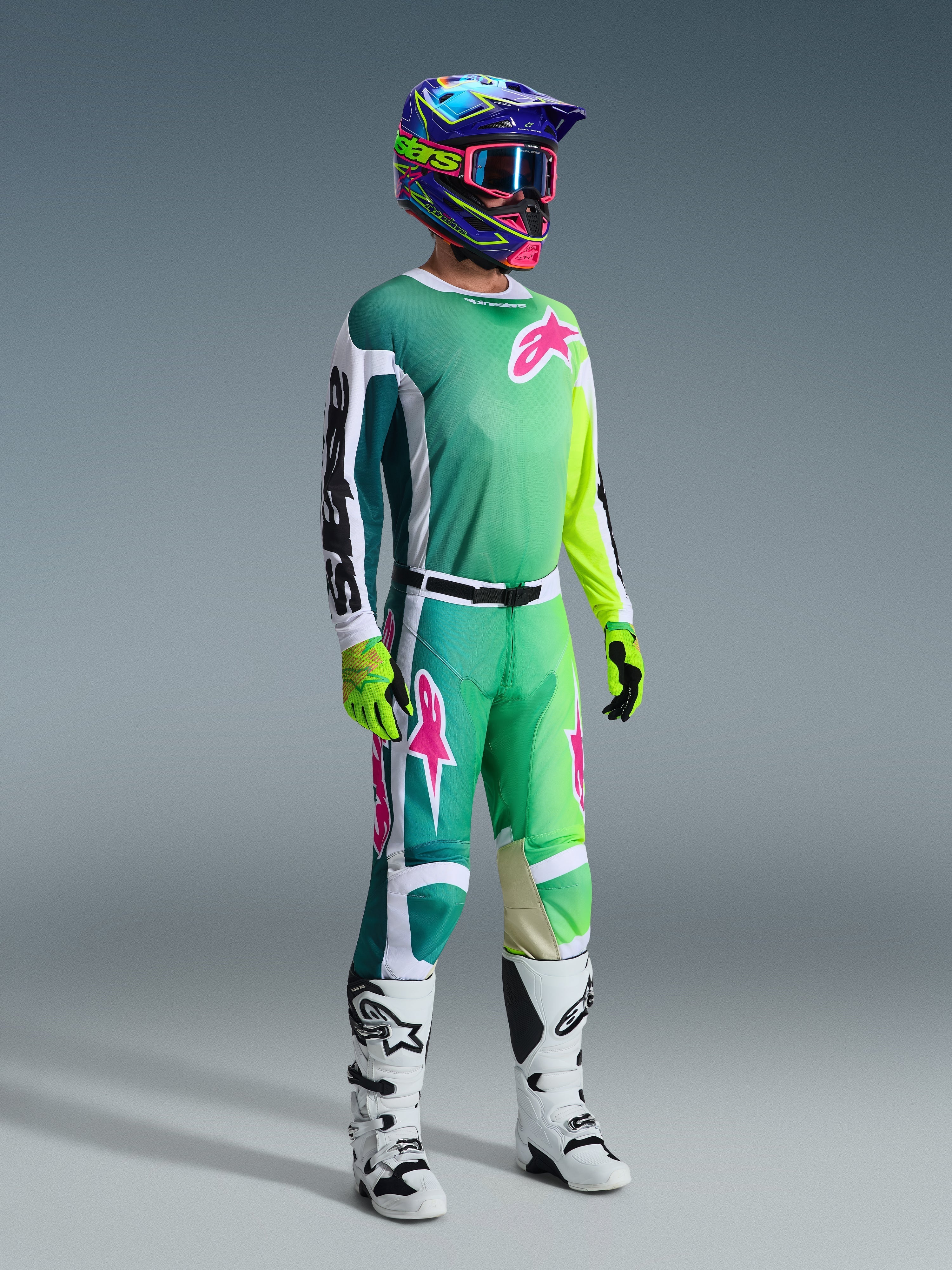 Motocross-Fahrer in kompletter Rennausrüstung, 2026 Racer Portl Trikot in Grün mit weiß-schwarzen Ärmeln und pinkfarbenem Logo, passende grüne Hose mit pinkfarbenen Akzenten, mehrfarbiger Helm mit Brille, weiß-schwarze Stiefel und grüne Handschuhe, abgestimmtes Outfit für den Offroad-Rennsport
