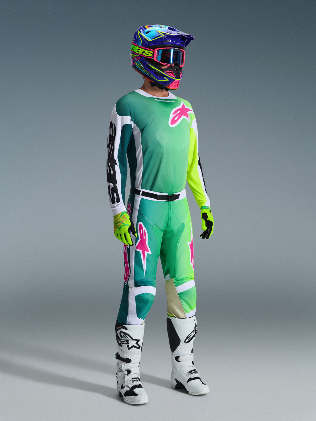 Alpinestars 2026 Racer Portl Gear Set, Motocross rider in teal to lime green gradient jersey with pink logos and white sleeves, matching green and white pants, colorful graphic helmet with pink goggles, white boots, and fluorescent yellow gloves, professional off-road racing kit.