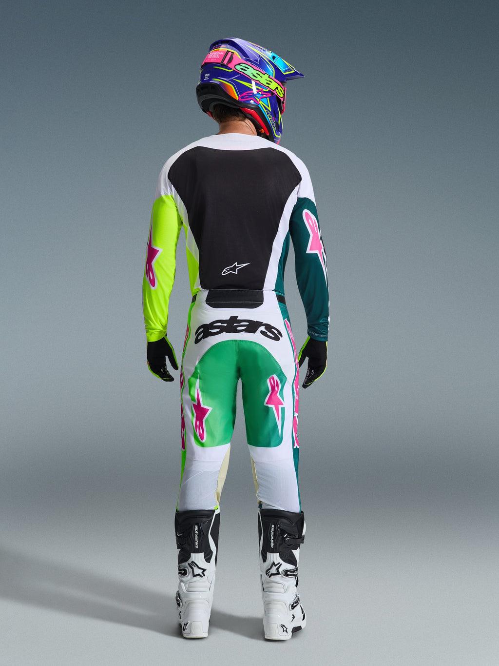 Motocross-Fahrer in der Rückansicht, trägt das 2026 Racer Portl Trikot in Green White Black, mit schwarzer Rückenpartie und asymmetrischen grünen Ärmeln mit pinkfarbenen Stern-Logos, kombiniert mit passender Motocross-Hose und weißen Stiefeln.