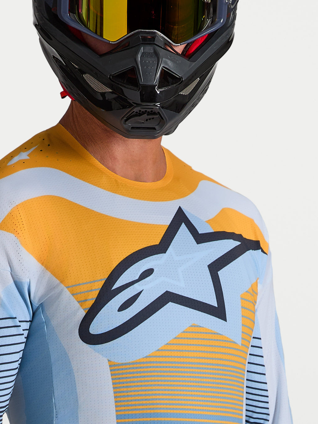 Alpinestars Techstar Maven Trikot in Blau und Orange, athletisches MX-Oberteil mit Belüftung, getragen mit einem MX-Helm.