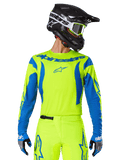 Alpinestars 2025 Fluid Haul Jersey, Motocross-Trikot, Neongelb und Blau, mit blauem Alpinestars-Branding auf der Brust, getragen mit passender Ausrüstung einschließlich eines schwarzen Helms und blauer Handschuhe, sportliche Passform für das Offroad-Fahren