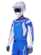 Motocross rider wearing the Alpinestars 2025 Fluid Haul Gear Set in Blue and White, featuring a blue jersey with white accents, matching blue pants with star logos, a white helmet with blue goggles, and coordinated blue and grey gloves, complete off-road racing outfit.