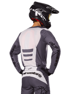 Motocross-Fahrer von hinten in Alpinestars 2025 Fluid Haul Gear Set, grau-weißes Trikot und Hose, schwarzer Helm mit weißen Grafiken, gelbe Brille, abgestimmtes Motocross-Rennoutfit