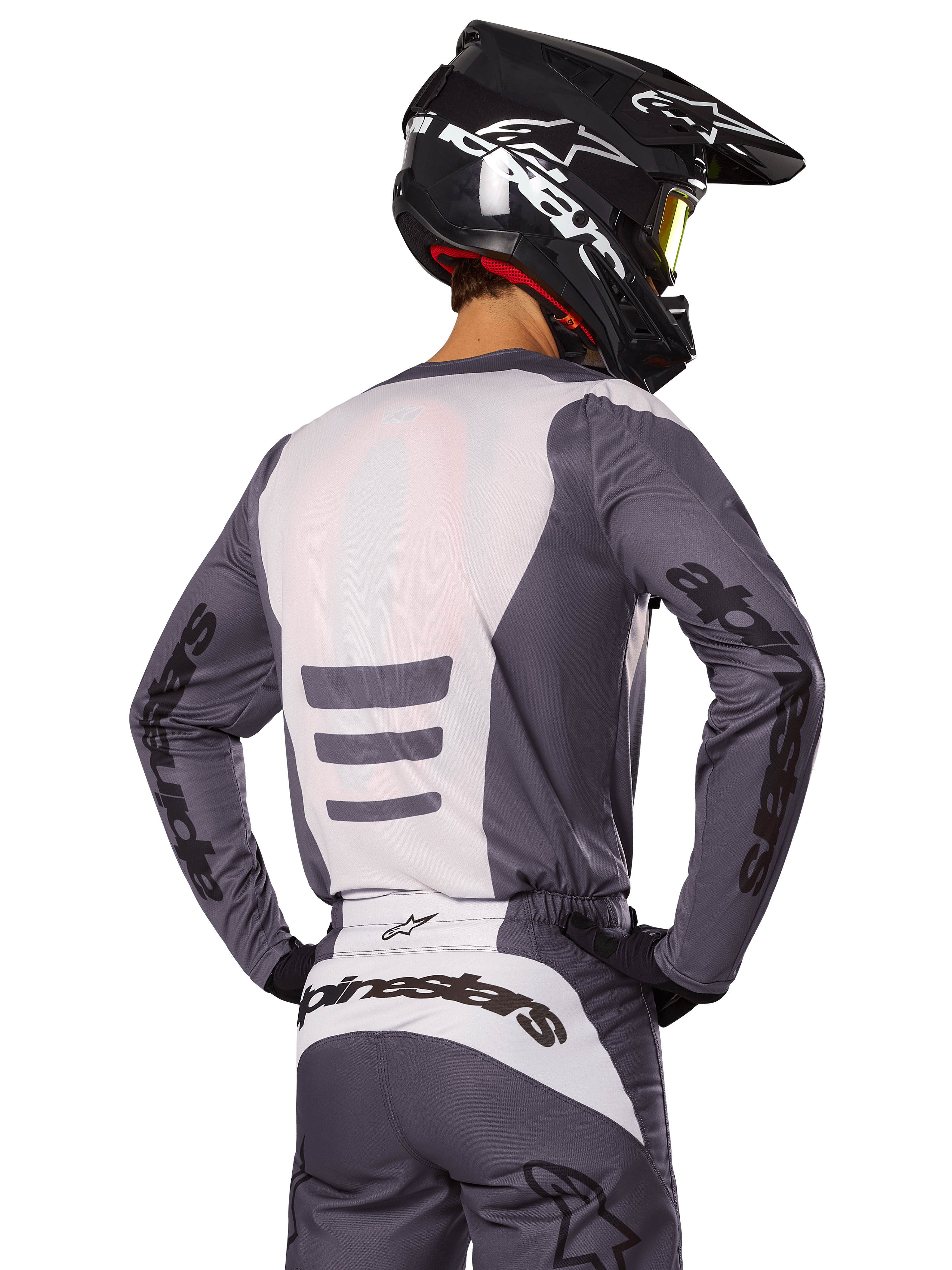 Motocross-Fahrer von hinten in Alpinestars 2025 Fluid Haul Gear Set, grau-weißes Trikot und Hose, schwarzer Helm mit weißen Grafiken, gelbe Brille, abgestimmtes Motocross-Rennoutfit