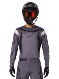 Motocross-Fahrer im 2025 Fluid Haul Jersey und Gear Set, Grau mit schwarzen und weißen Akzenten, langärmelig mit markantem Branding, schwarzer Helm mit orangener Brille und schwarze Handschuhe, aufeinander abgestimmtes Outfit für Offroad-Rennsport