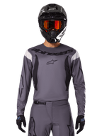Motocross-Fahrer im 2025 Fluid Haul Jersey und Gear Set, Grau mit schwarzen und weißen Akzenten, langärmelig mit markantem Branding, schwarzer Helm mit orangener Brille und schwarze Handschuhe, aufeinander abgestimmtes Outfit für Offroad-Rennsport