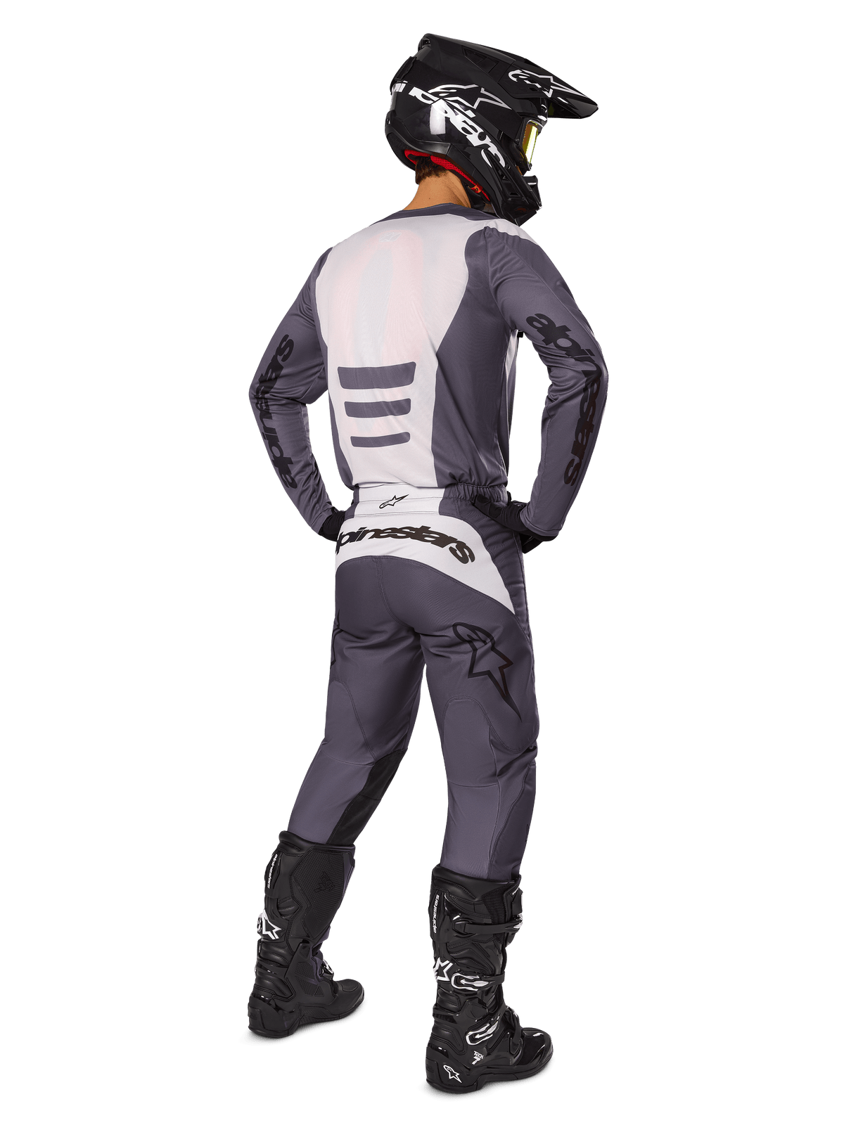 Motocross-Fahrer von hinten im Alpinestars 2025 Fluid Haul Ausrüstungsset, grau-weißes Trikot und passende Hose, schwarzer Helm mit gelber Brille, schwarze Motocross-Stiefel, komplette Rennausrüstung für Offroad-Performance