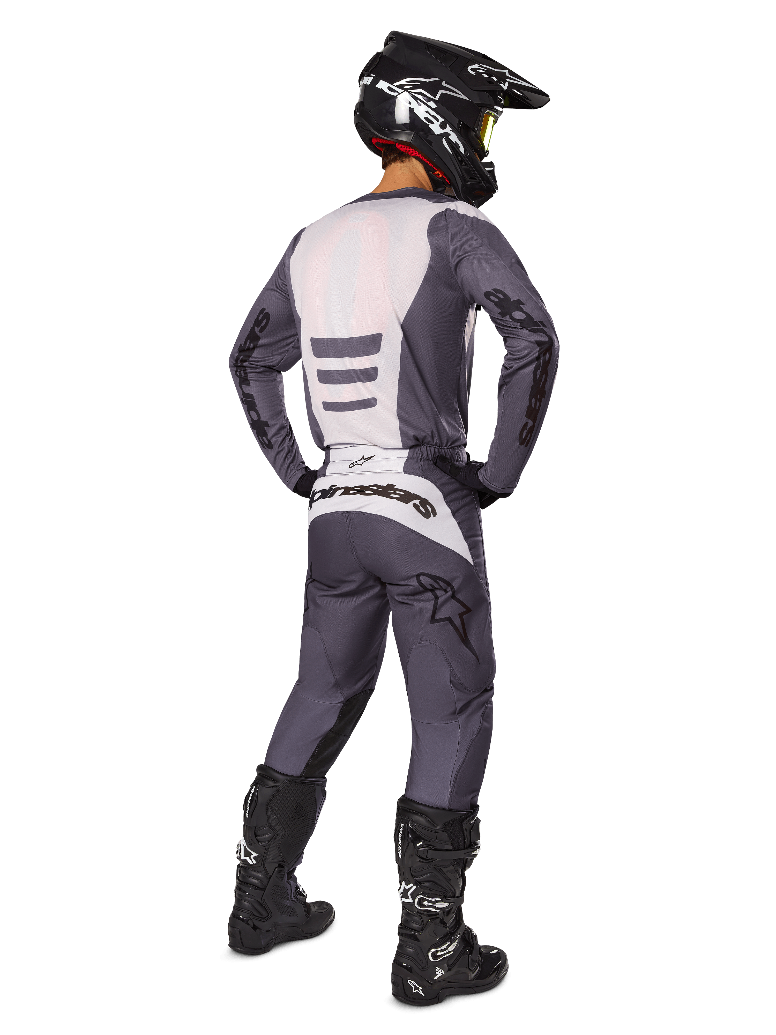 Motocross-Fahrer von hinten im Alpinestars 2025 Fluid Haul Ausrüstungsset, grau-weißes Trikot und passende Hose, schwarzer Helm mit gelber Brille, schwarze Motocross-Stiefel, komplette Rennausrüstung für Offroad-Performance