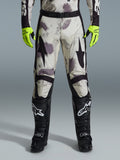 Alpinestars 2026 Racer Lahnd Hose, Motocross-Hose, Sand-Camo-Muster mit grauen und lila abstrakten Grafiken, getragen mit neongelben Handschuhen und schwarzen Stiefeln, schwarze Stern-Logos auf den Oberschenkeln und ein schwarzer Taillengürtel, strapazierfähige Offroad-Rennausrüstung