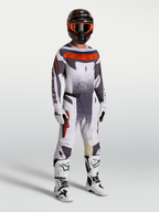 Alpinestars Techstar Swan Trikot und Gear Set am Model, Herren-Motocross-Outfit in Helllila, Grau und fluoreszierendem Rot.