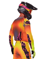 Motocross-Fahrer in der Rückseitenansicht im Alpinestars 2025 Supertech Lipan Gear Set, gelb-orange-roter Farbverlauf mit schwarzem und pinkem Branding, schwarzer Helm mit pinken Akzenten und oranger Brille, professionelle Offroad-Rennbekleidung.