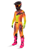 Motocross-Fahrer im Alpinestars Supertech Lipan Gear Set 2025, Trikot und Hose mit gelb-orangem Farbverlauf und pinken Akzenten, schwarzer Helm mit gelb-roter Brille, leuchtend gelbe Handschuhe und knallpinke Stiefel, abgestimmtes Offroad-Rennoutfit