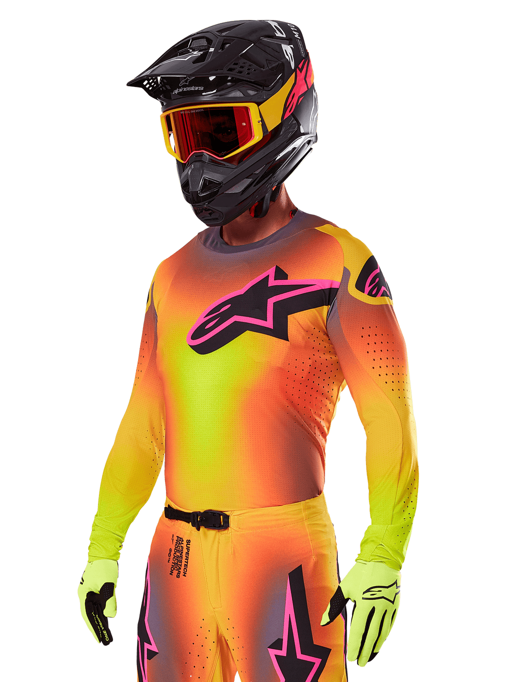 Motocross-Fahrer im Alpinestars 2025 Supertech Lipan Ausrüstungsset, Trikot mit gelb-orangem Farbverlauf und pink-schwarzem Astars-Logo, neongelbe Handschuhe, schwarzer Helm mit roter Brille, professionelle Offroad-Rennausrüstung