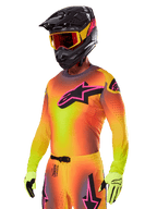 Motocross-Fahrer im Alpinestars 2025 Supertech Lipan Ausrüstungsset, Trikot mit gelb-orangem Farbverlauf und pink-schwarzem Astars-Logo, neongelbe Handschuhe, schwarzer Helm mit roter Brille, professionelle Offroad-Rennausrüstung