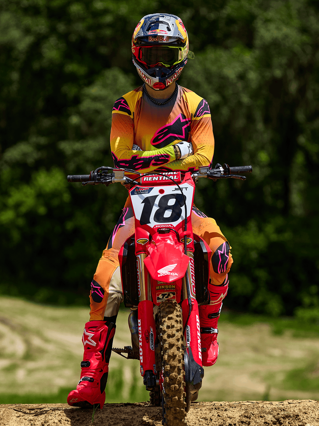 Motocross-Fahrer auf einem roten Honda Dirtbike mit Startnummer 18, Alpinestars 2025 Supertech Lipan Trikot und passende Hose in Gelb und Pink, leuchtend pinke Alpinestars Stiefel, Red Bull Helm, professionelle Rennausrüstung für Offroad-Performance