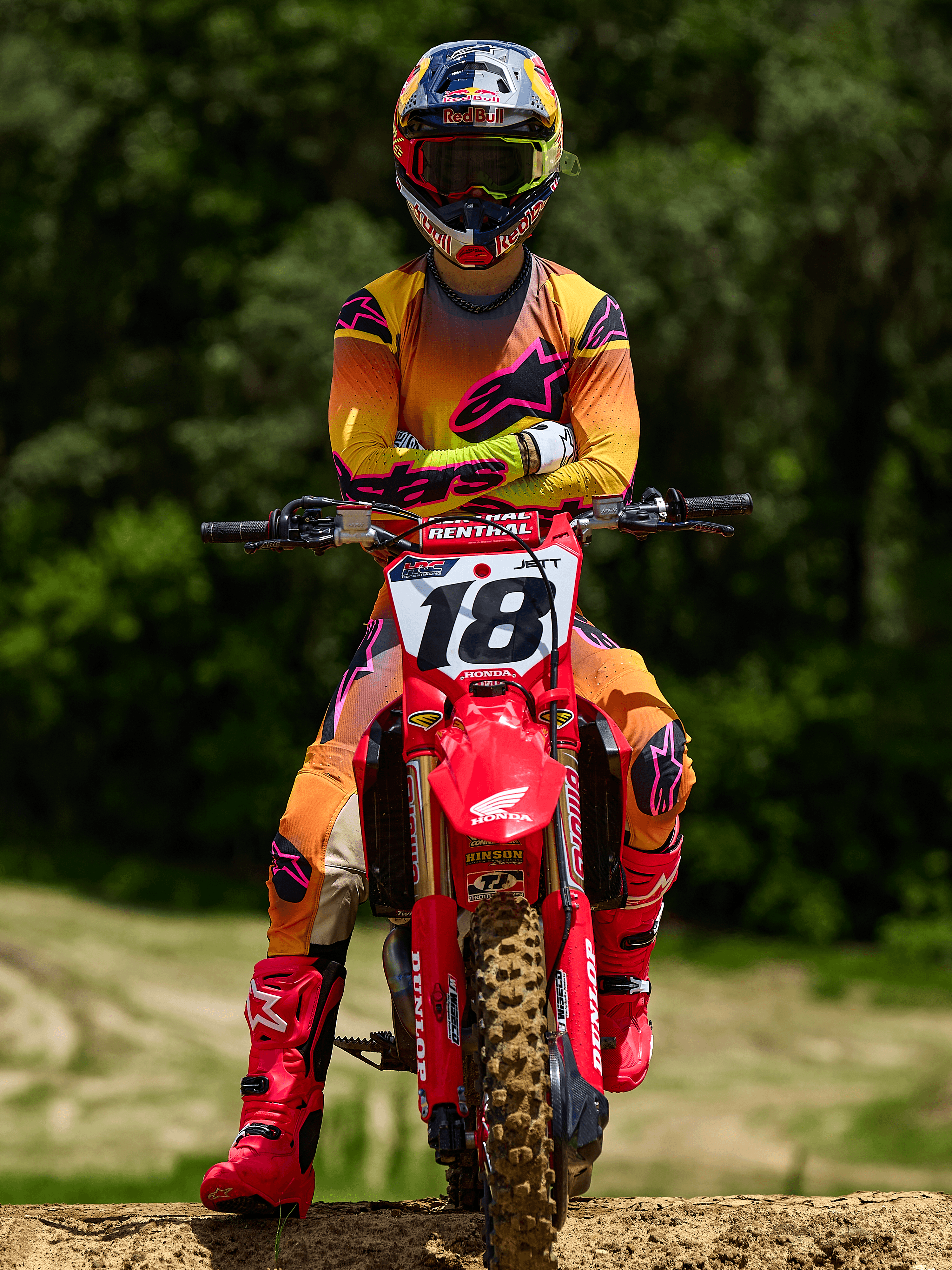 Motocross-Fahrer auf einem roten Honda Dirtbike mit Startnummer 18, Alpinestars 2025 Supertech Lipan Trikot und passende Hose in Gelb und Pink, leuchtend pinke Alpinestars Stiefel, Red Bull Helm, professionelle Rennausrüstung für Offroad-Performance