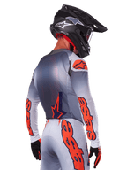 Motocross-Fahrer von hinten im Alpinestars 2025 Supertech Lipan Trikot und Ausrüstungsset, Grau mit Orange Fluo Akzenten, markantes Branding auf Rücken und Ärmeln, schwarzer Helm und schwarze Handschuhe, koordiniertes Motocross-Rennoutfit