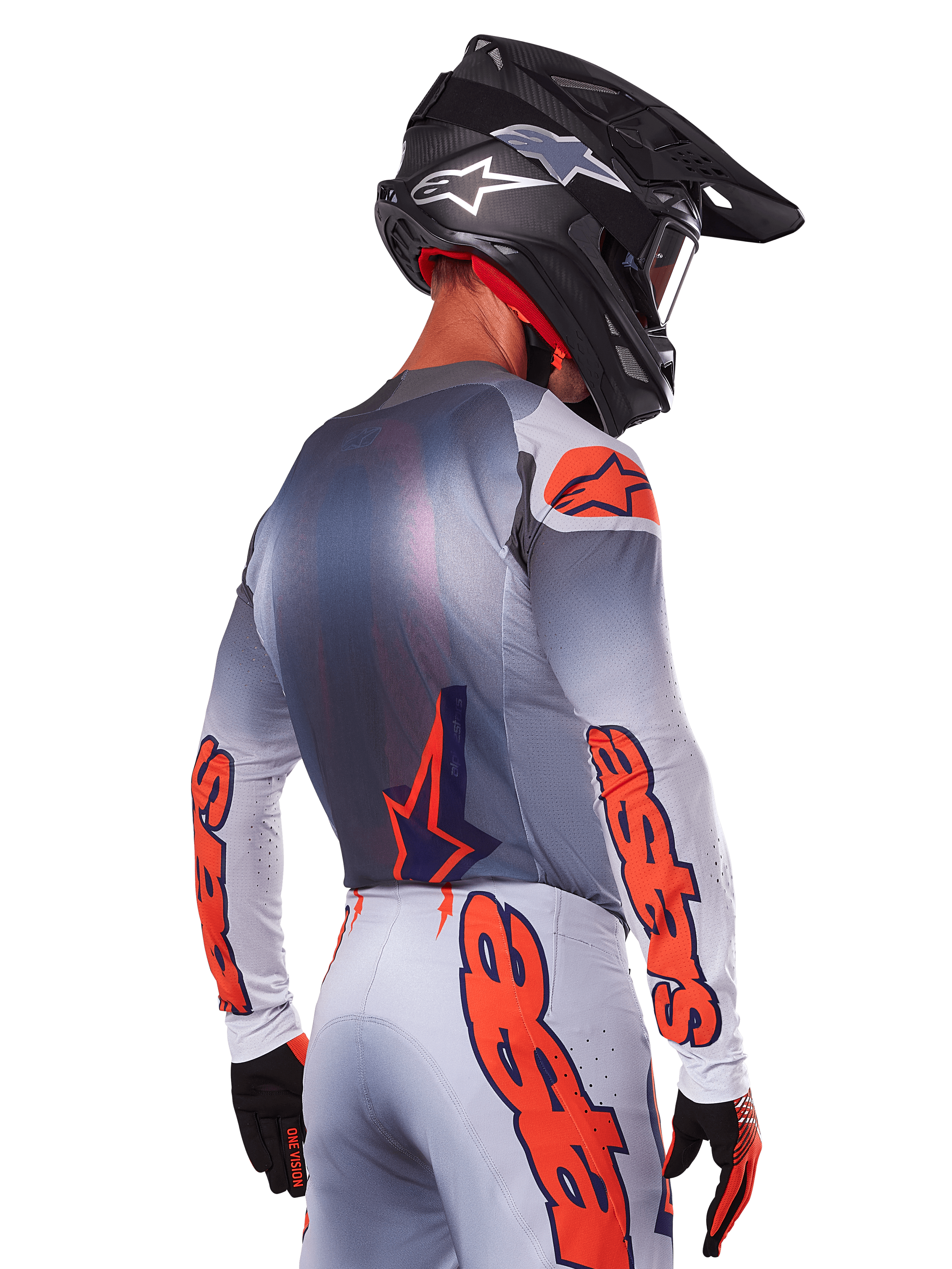 Motocross-Fahrer von hinten im Alpinestars 2025 Supertech Lipan Trikot und Ausrüstungsset, Grau mit Orange Fluo Akzenten, markantes Branding auf Rücken und Ärmeln, schwarzer Helm und schwarze Handschuhe, koordiniertes Motocross-Rennoutfit