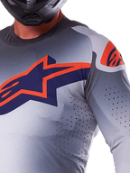 Alpinestars 2025 Supertech Lipan Trikot, Motocross-Trikot, Grau Orange Fluo, mit großem marineblauem und orangem Stern-Logo auf der Brust, lasergeschnittenen Perforationen für Luftzirkulation, leichte Mesh-Konstruktion, getragen mit einem schwarzen Helm