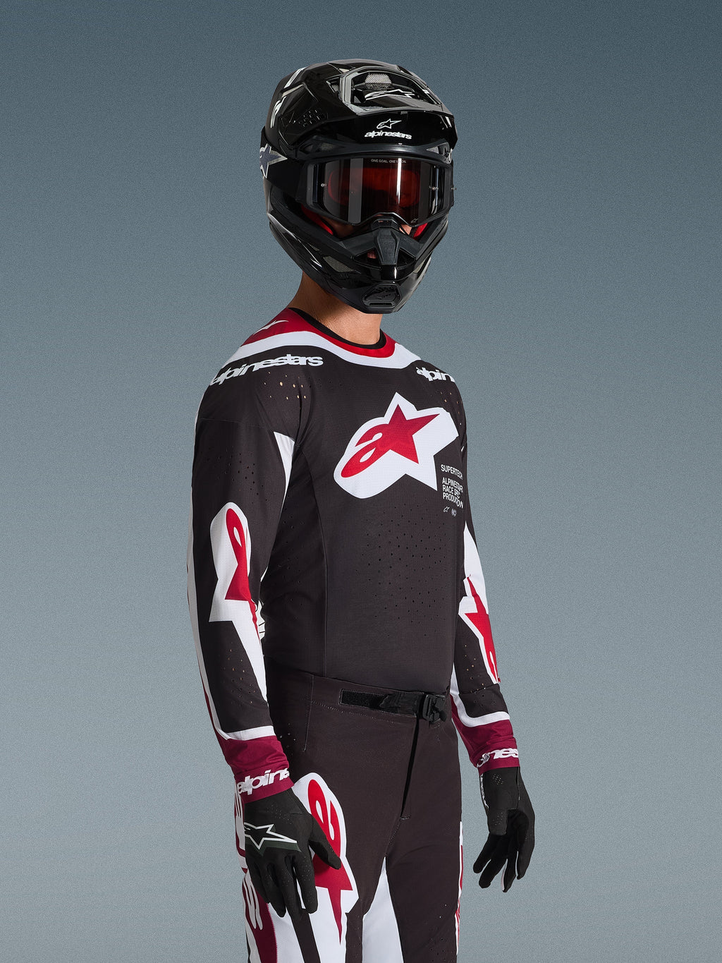 Alpinestars 2026 Supertech AFD Vista Jersey, Motocross rider wearing complete racing gear, Black jersey with red and white accents, large logo on chest, laser-cut perforations, worn with matching pants, black helmet, and red goggles, coordinated outfit for off-road racing